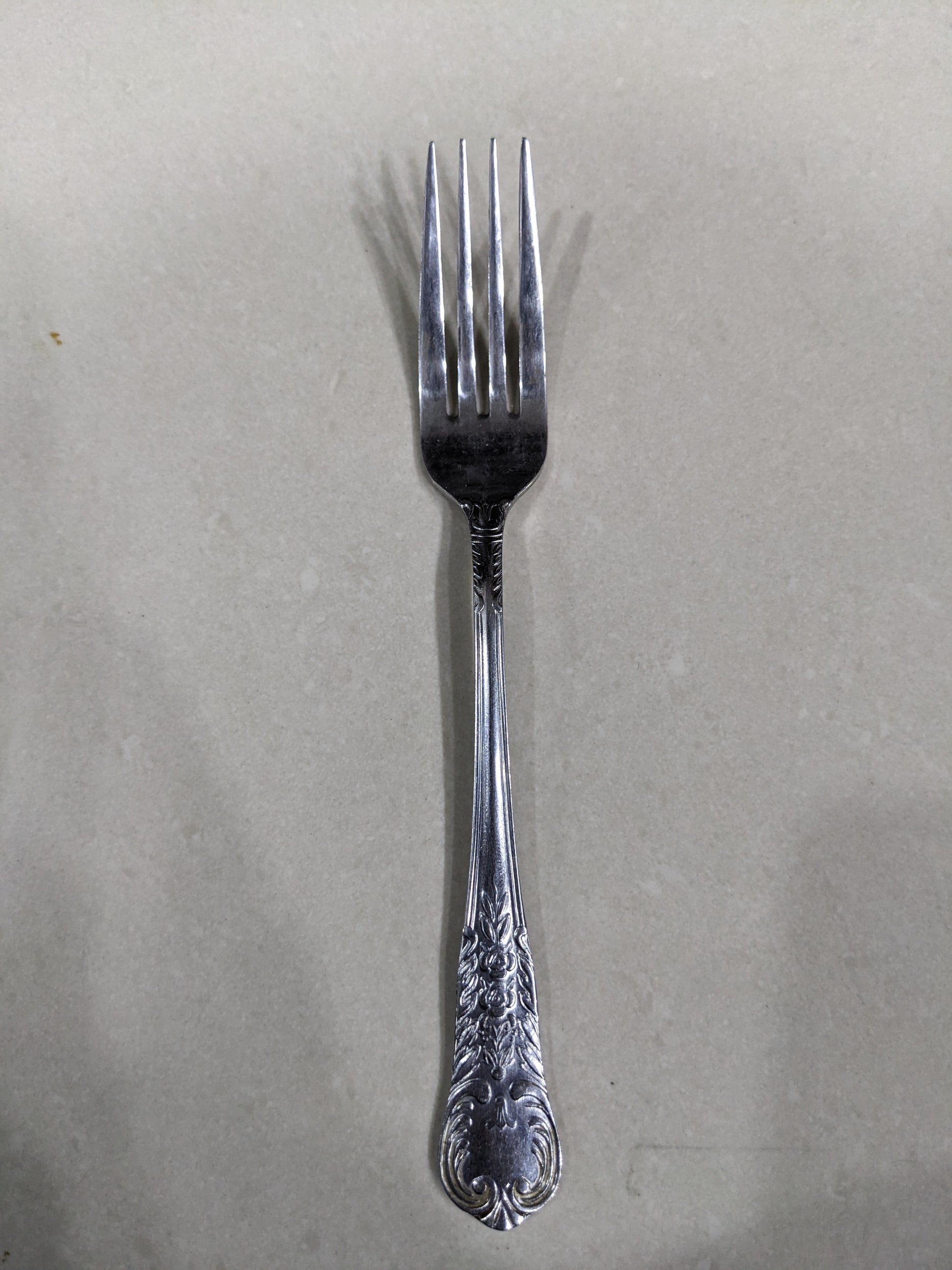 Close-up shot of a single vintage fork, showing the detailed floral engravings on the handle and the tines