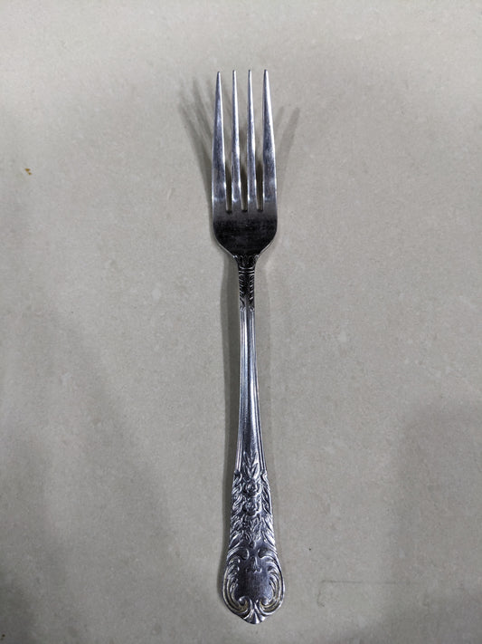 Close-up shot of a single vintage fork, showing the detailed floral engravings on the handle and the tines