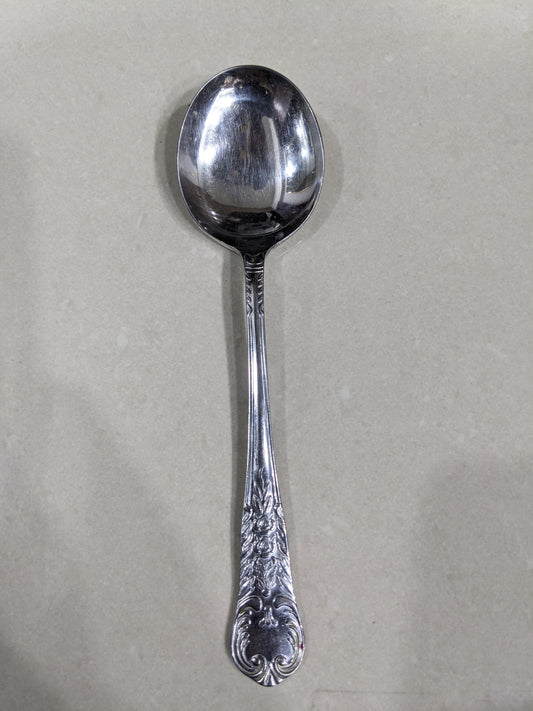 Close-up view of a single spoon from the set, highlighting the floral and scroll handle engravings